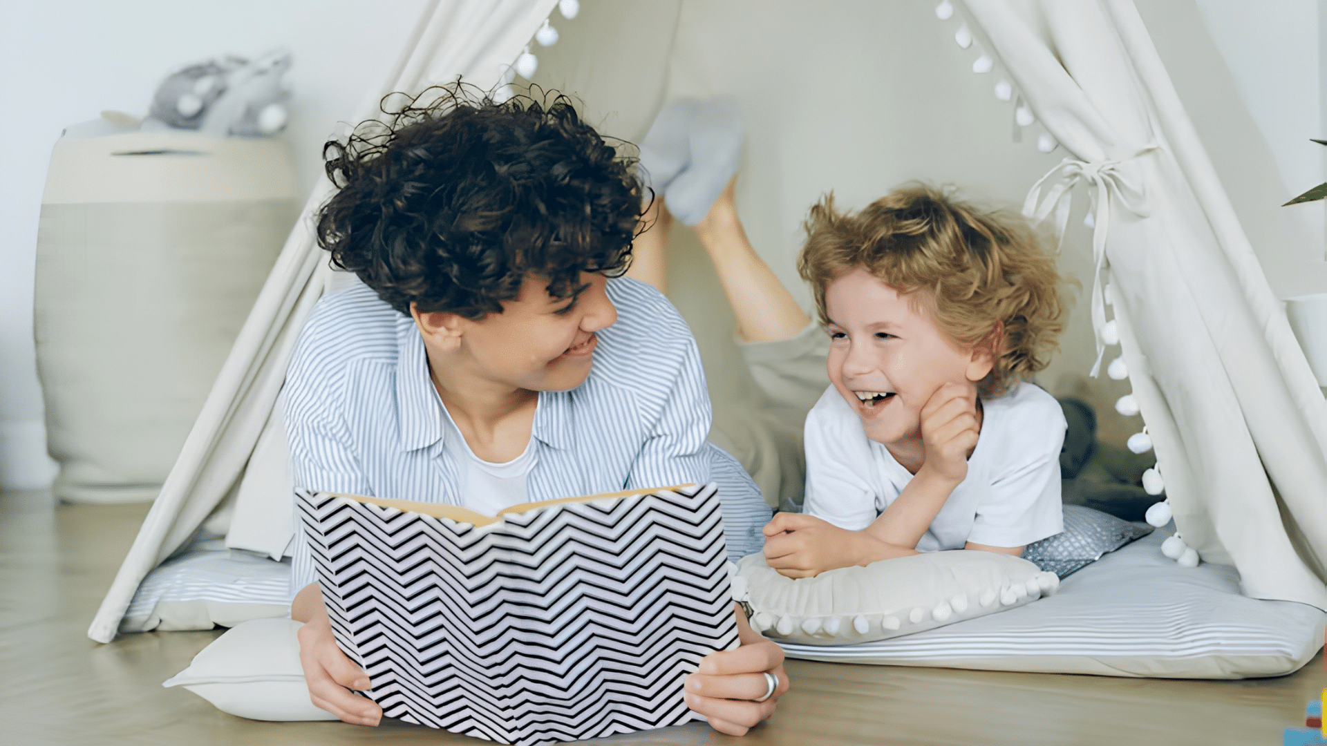 adult and child laughing together while reading a book inside a play tent at home