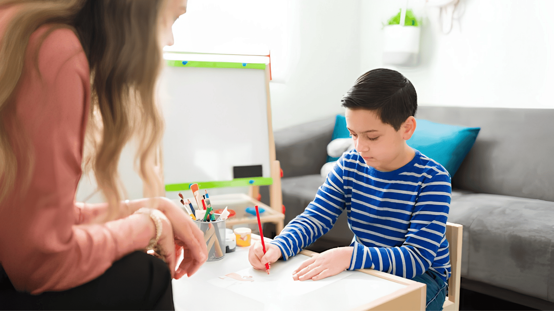 child drawing at a table while an adult observes and supports the activity at home