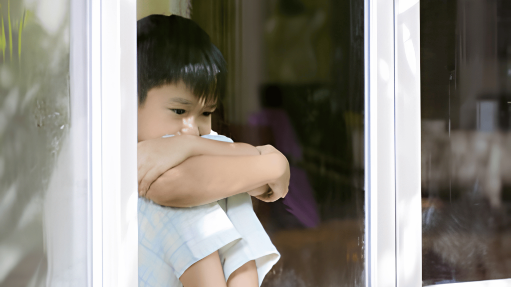 child sitting alone by window appearing sad during family separation and emotional stress at home