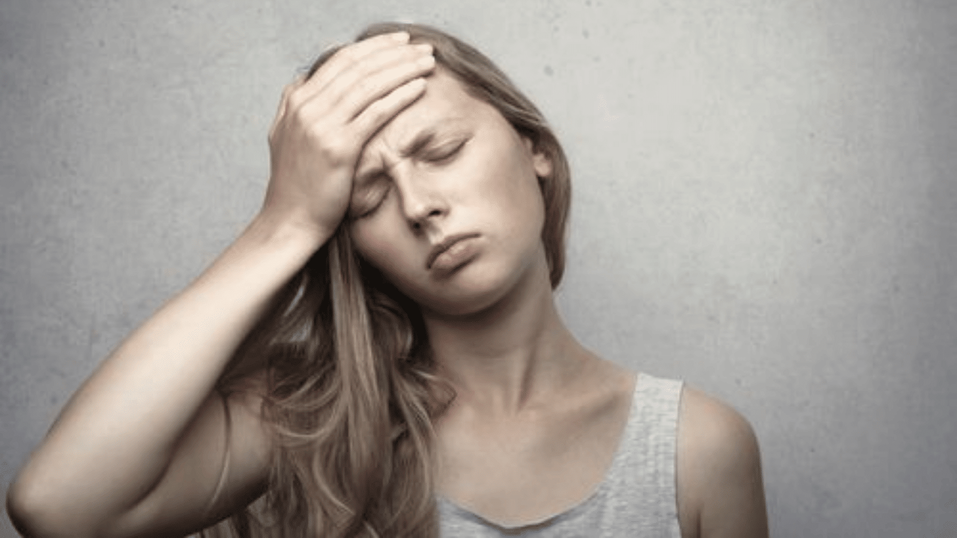 a woman holds her forehead with eyes closed appearing unwell and fatigued