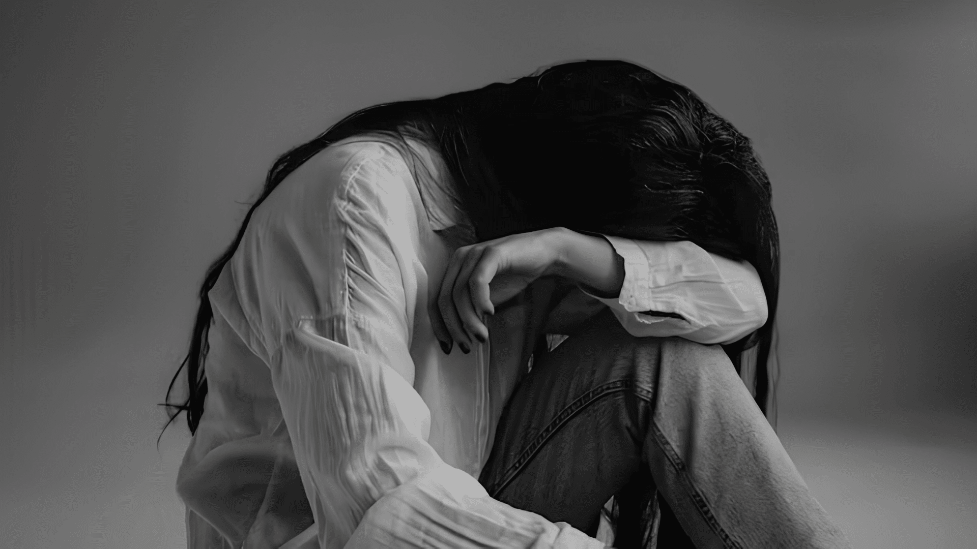a woman sits curled up with head resting on her arm showing sadness and emotional distress