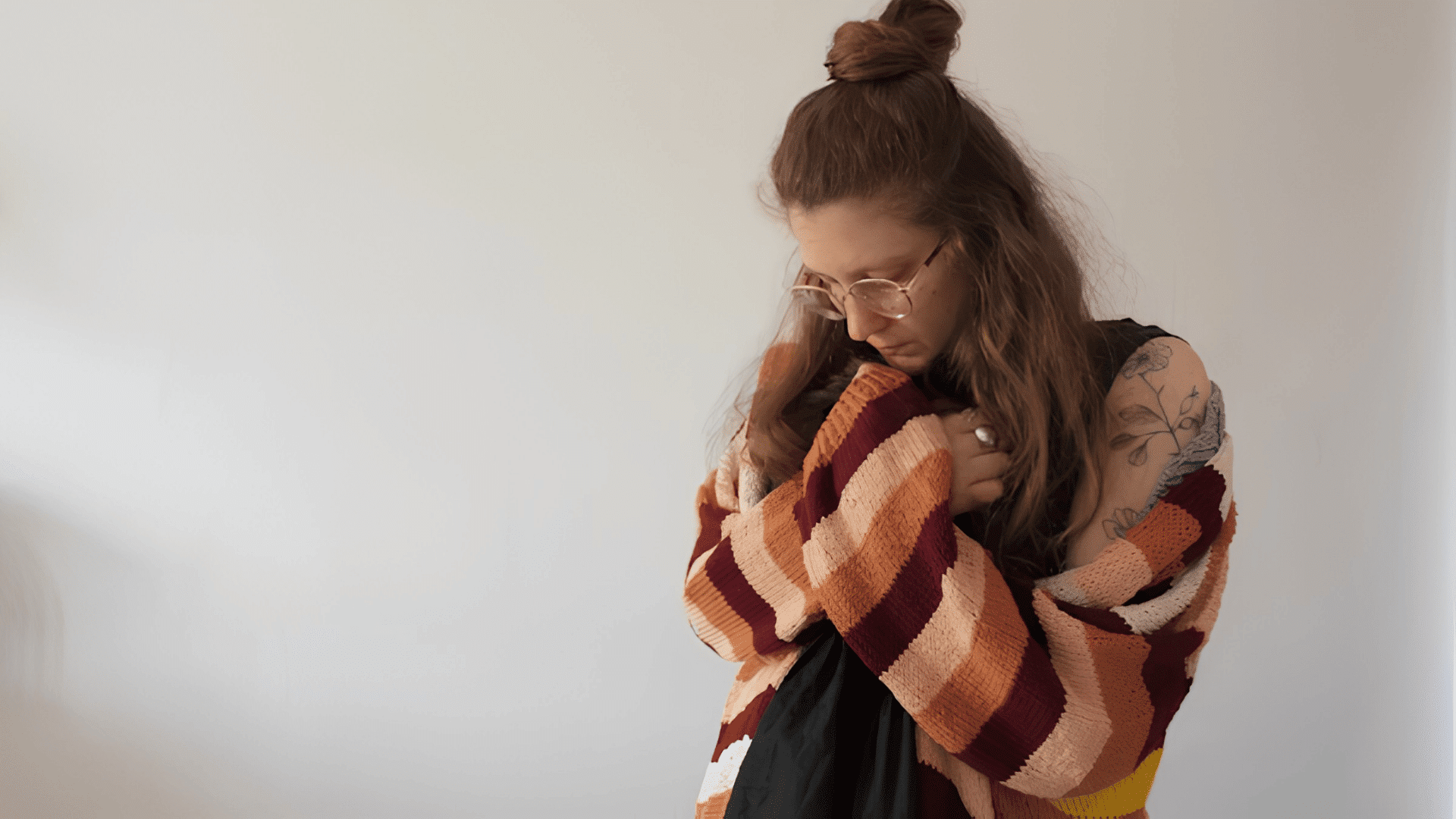 a woman wearing glasses hugs herself while looking down appearing anxious and withdrawn
