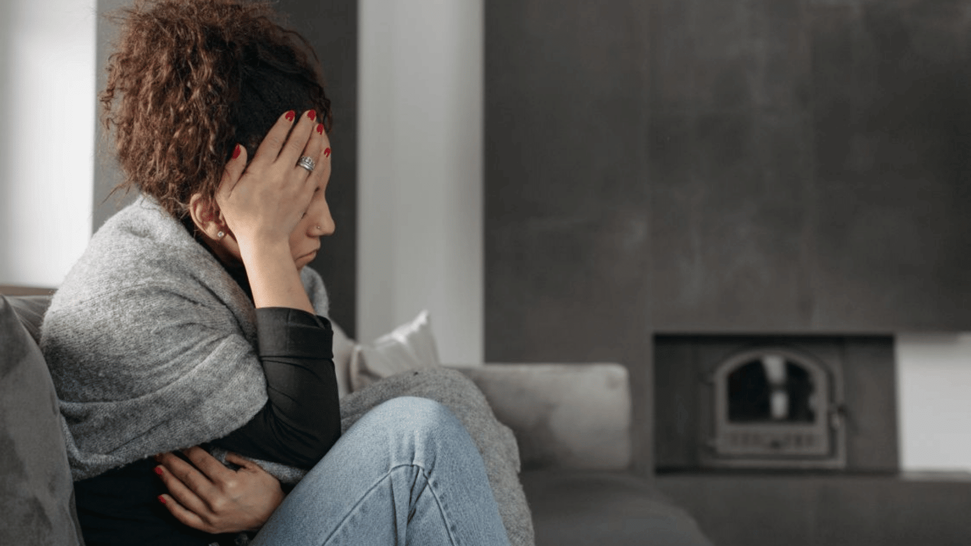 a woman wrapped in a blanket sits on a sofa appearing stressed and emotionally drained