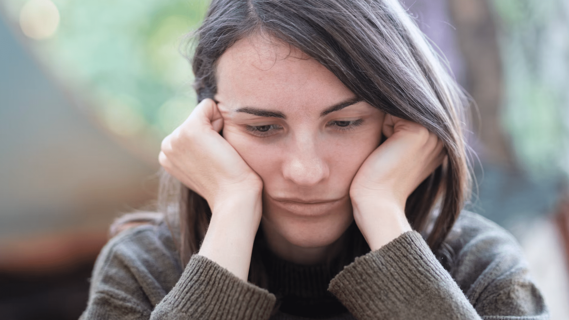 close up of a sad looking woman resting her chin in both hands with a worried expression