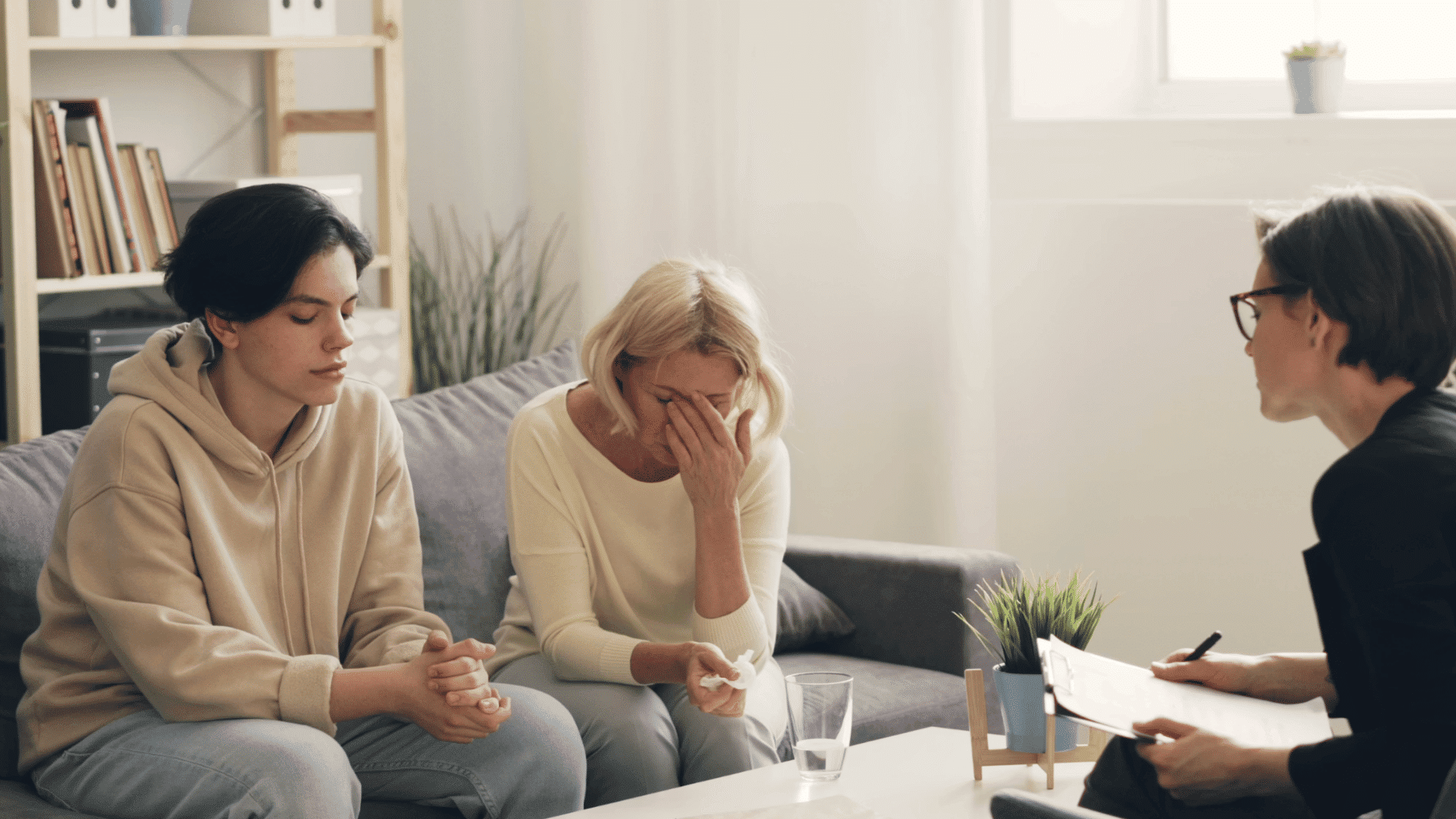 counselor speaking with a distressed woman and a young person during a supportive therapy session in a calm office
