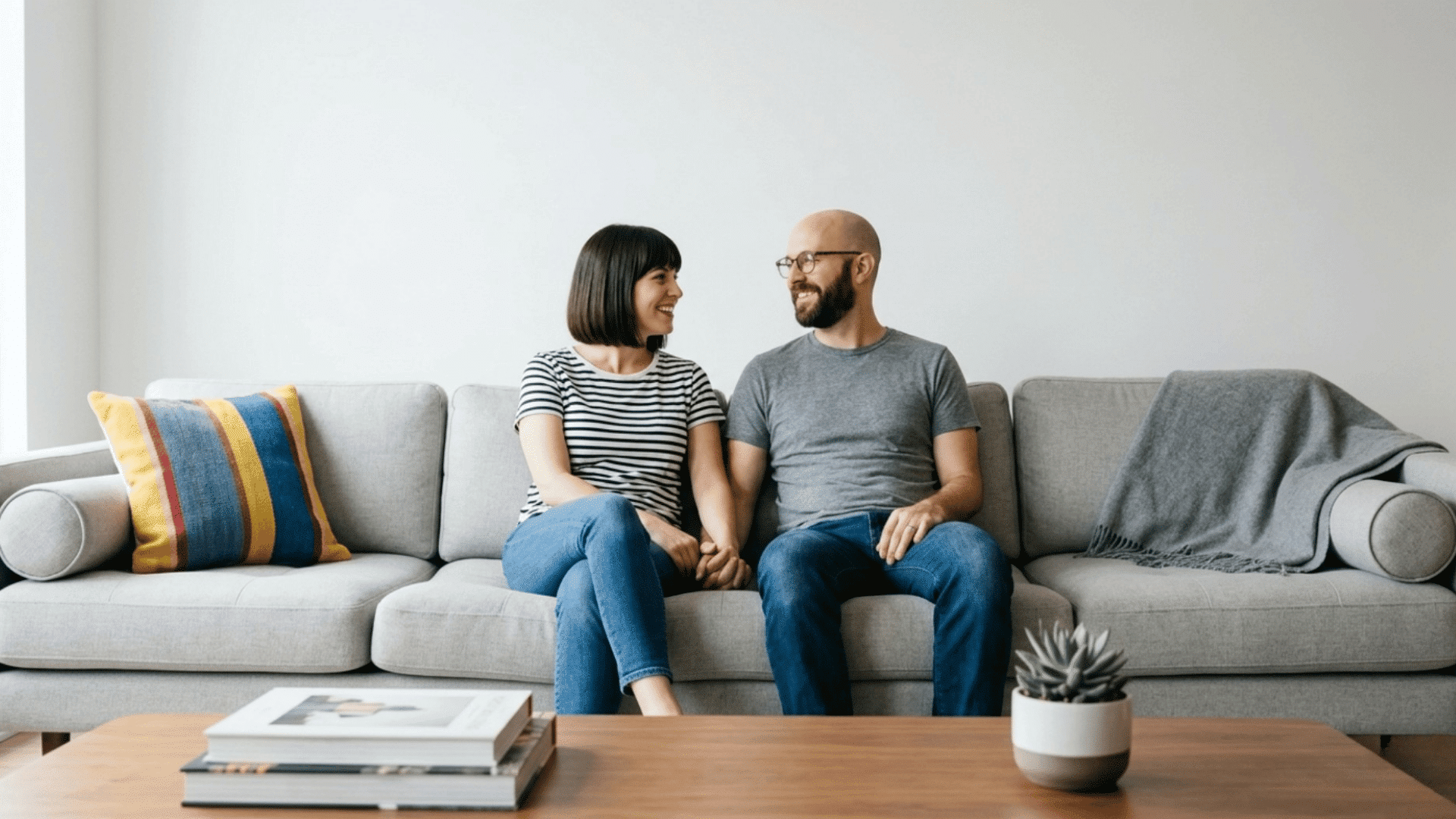 couple sitting on sofa holding hands and smiling at each other in living room