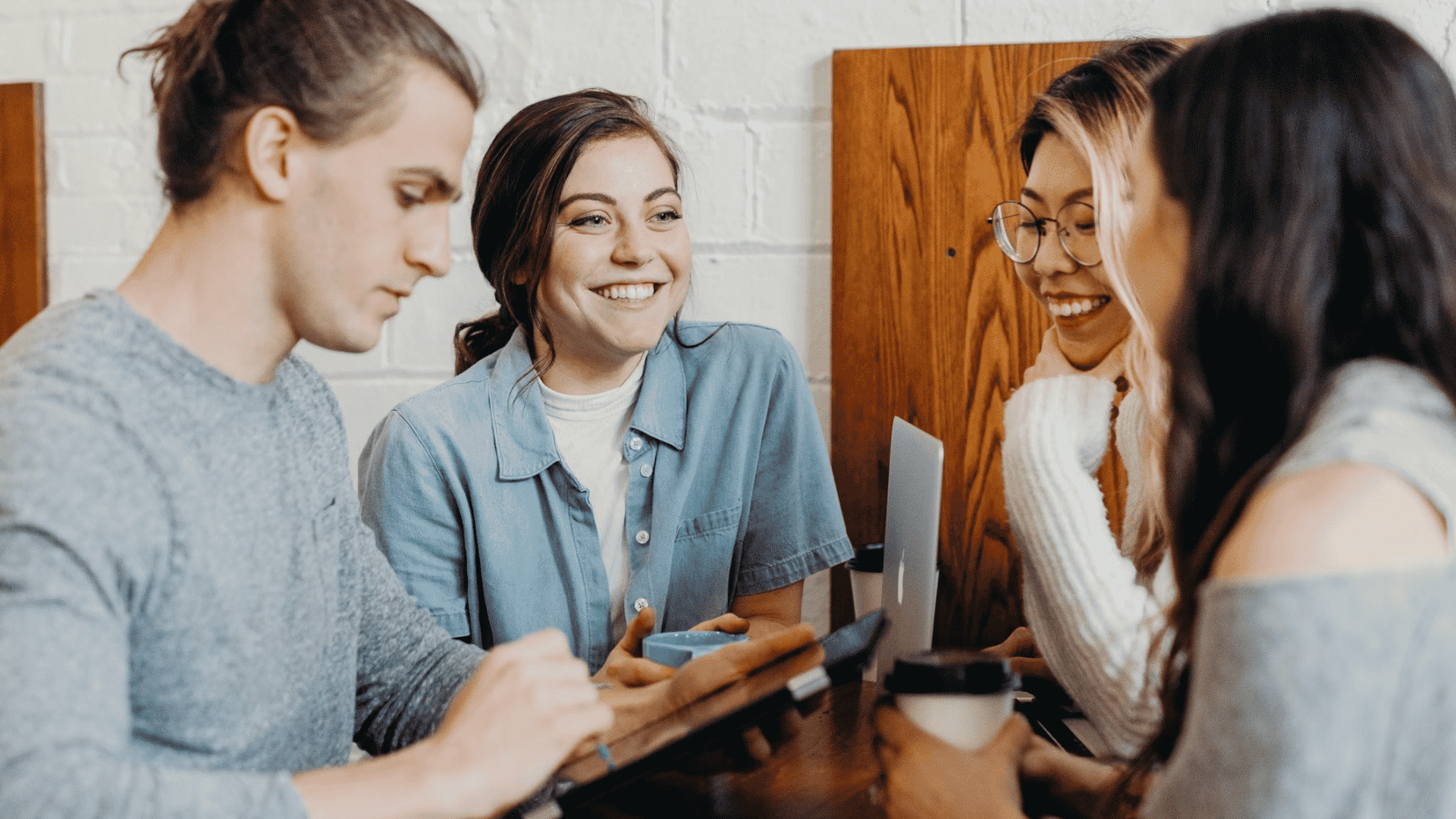 group of coworkers smiling and collaborating around a table with laptops coffee and a tablet during a team meeting