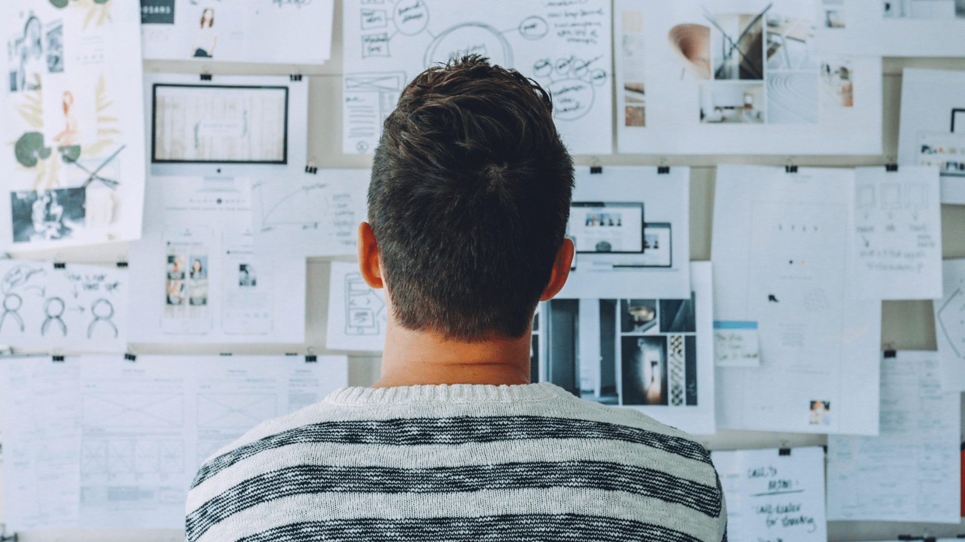man from behind looking at a wall covered in notes and sketches