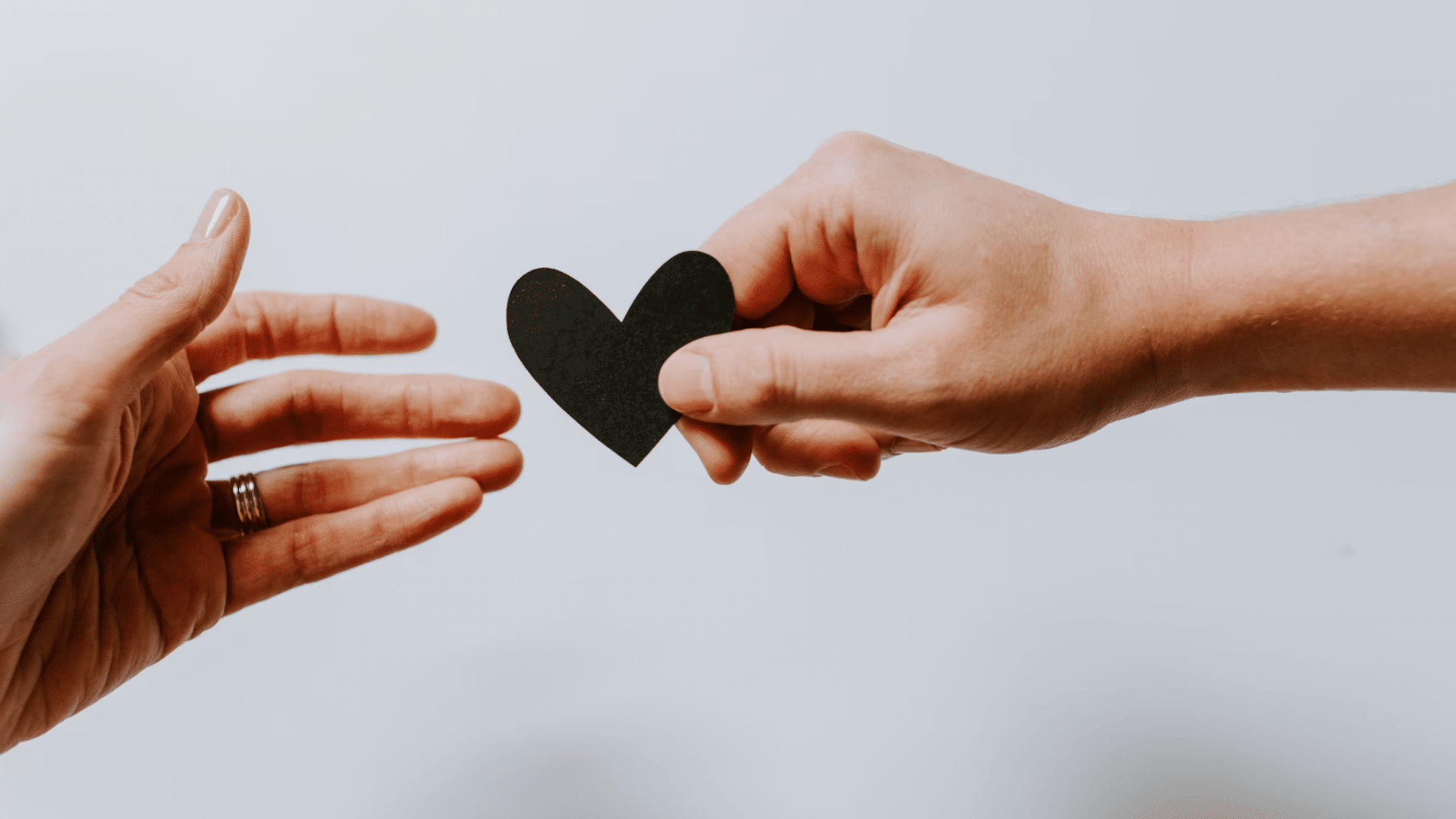 one hand offering a black heart shape to another hand symbolizing support care and compassion