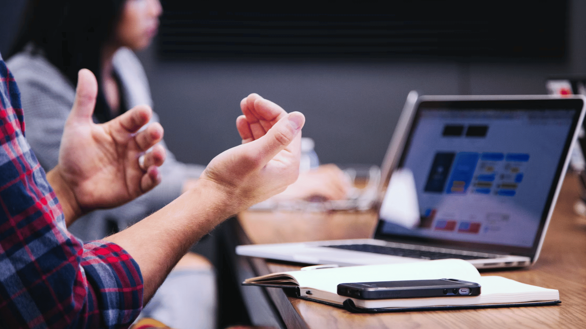 person gesturing while discussing ideas beside a laptop and notebook during a collaborative meeting in an office