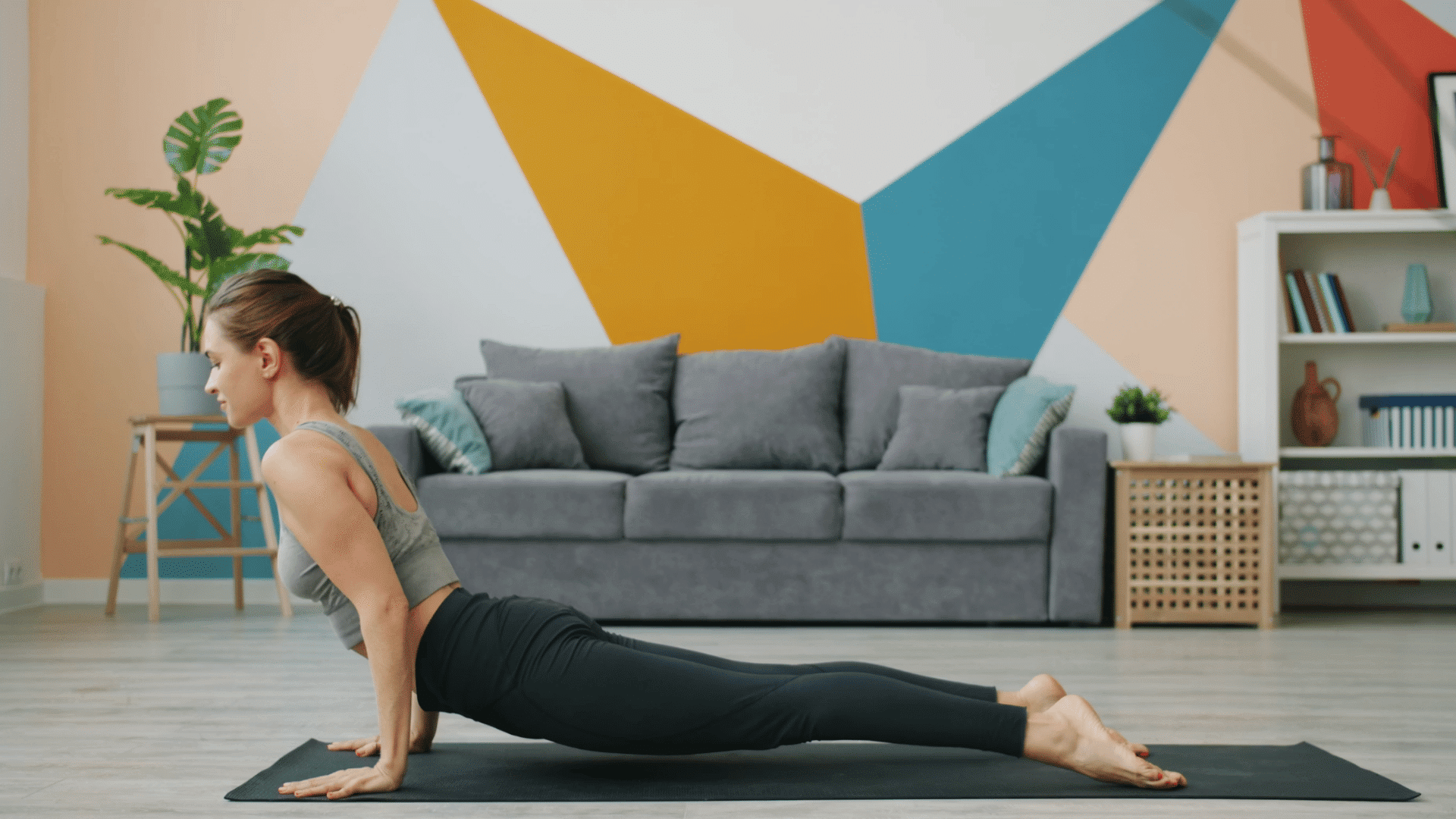 person practicing upward facing dog yoga pose on a mat in a modern living room with a colorful geometric wall mural