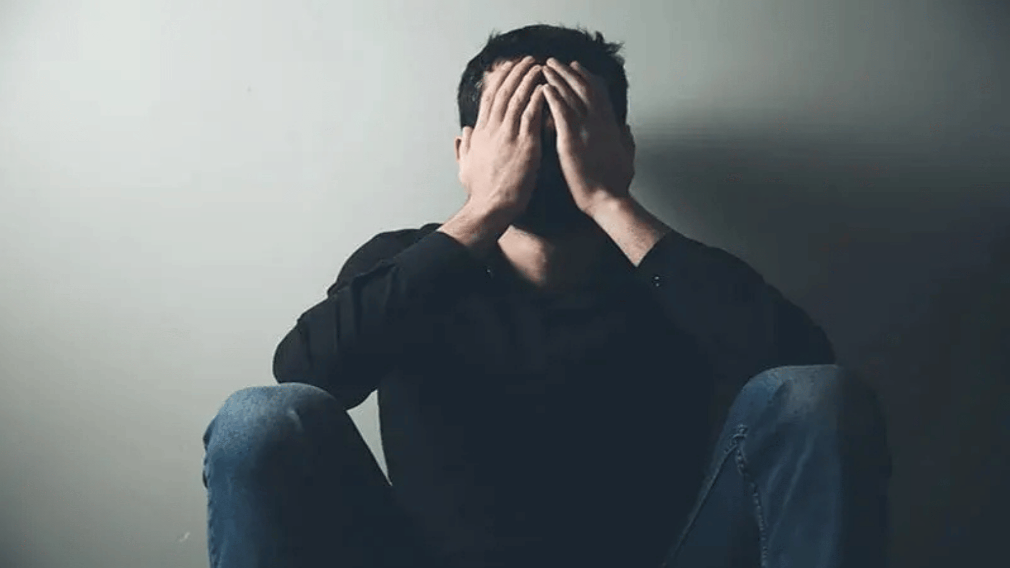 person sitting alone with hands covering face showing emotional pain stress and symptoms commonly linked to betrayal trauma