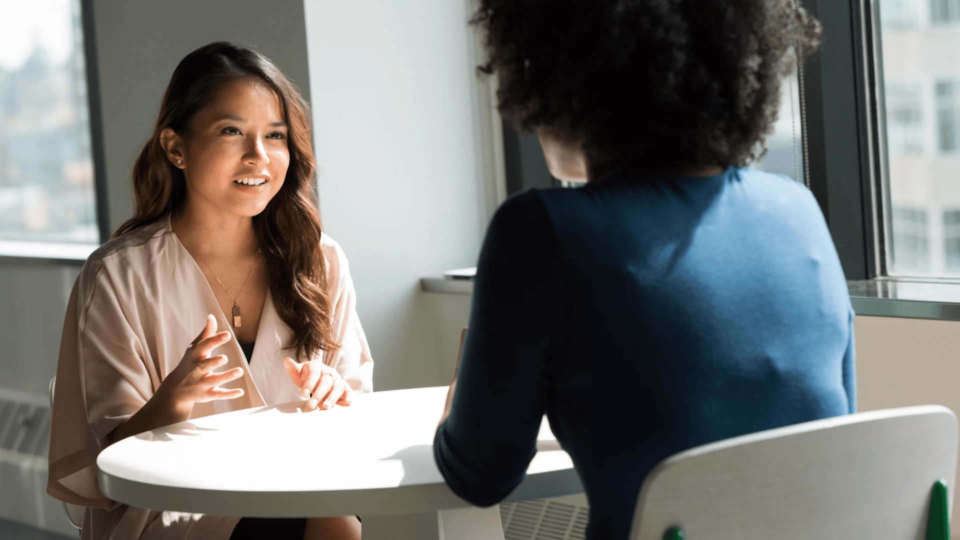 person speaking with another person across a table during a friendly meeting in a bright office with natural window light