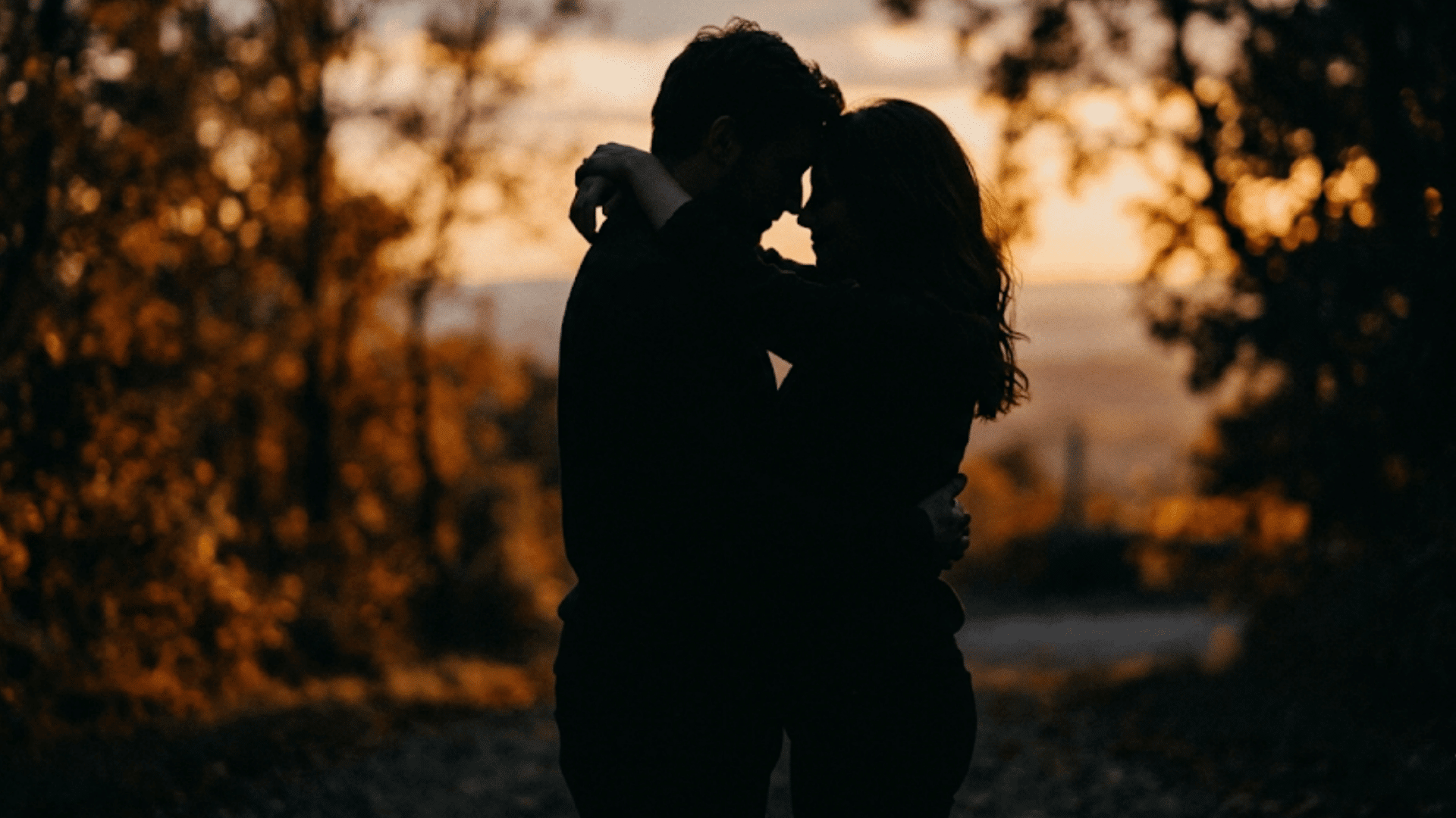 silhouetted couple embracing on a quiet path at sunset surrounded by softly blurred trees and warm light