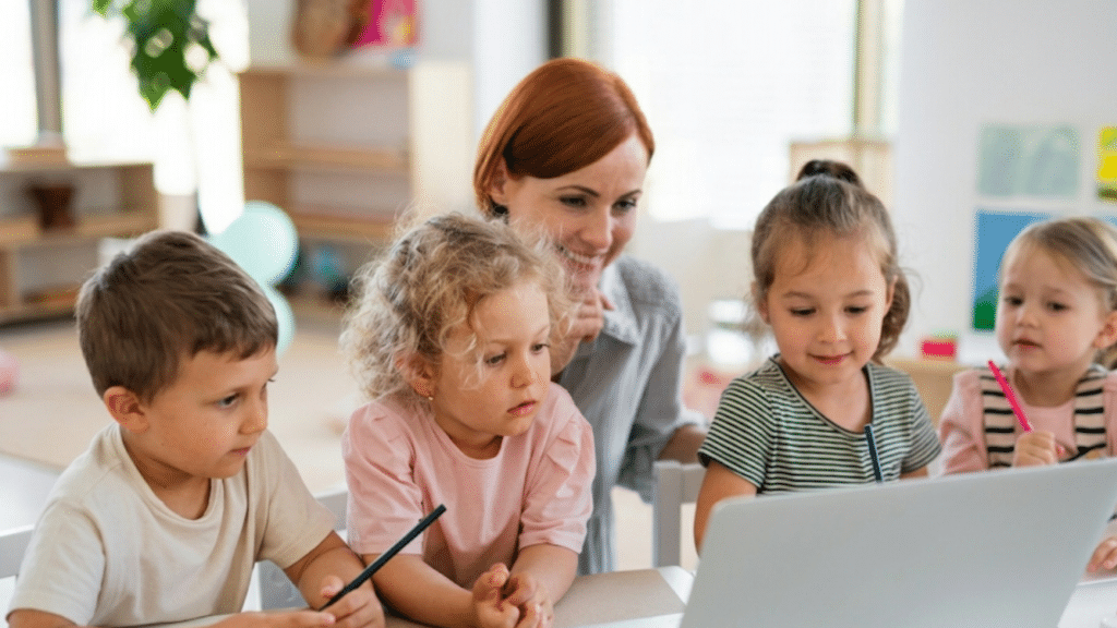 teacher guiding four young children gathered around a laptop during a creative classroom learning activity