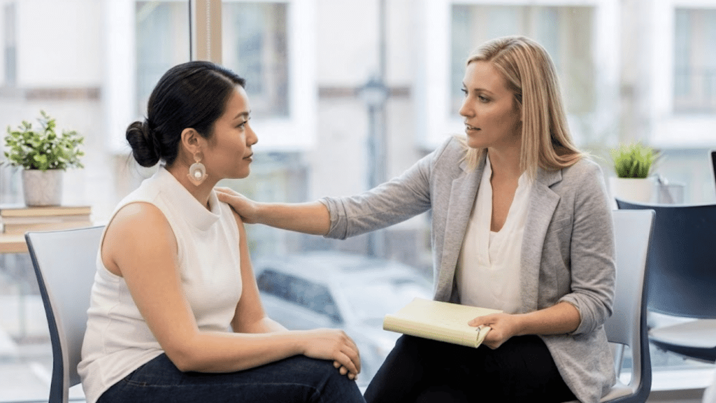 two women seated in an office having a supportive conversation with one woman gently touching the others shoulder