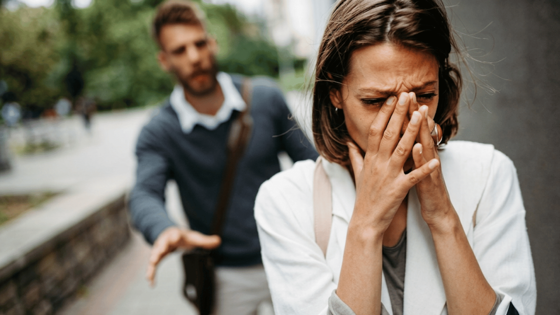 woman crying after rejection while a man reaches toward her on a quiet city sidewalk after a hard talk