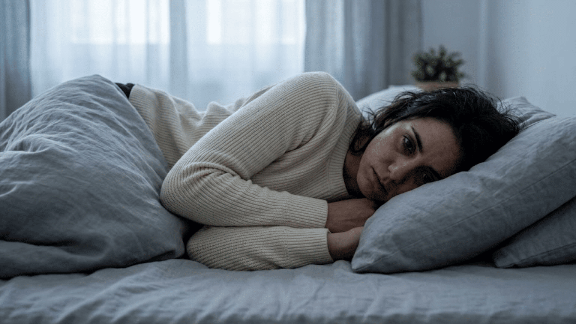 woman lying awake on a bed resting her head on a pillow with a thoughtful expression in a softly lit bedroom