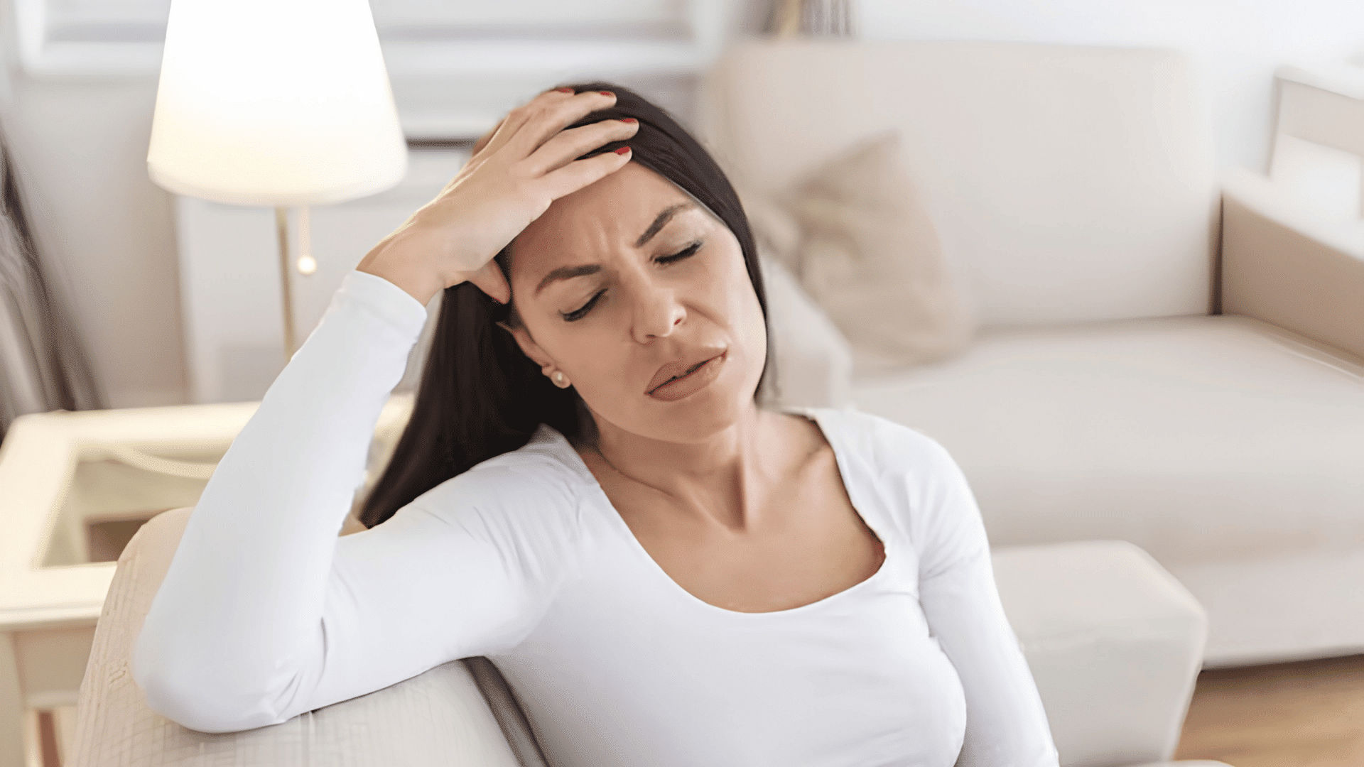 woman sitting on a sofa holding her forehead while appearing unwell at home