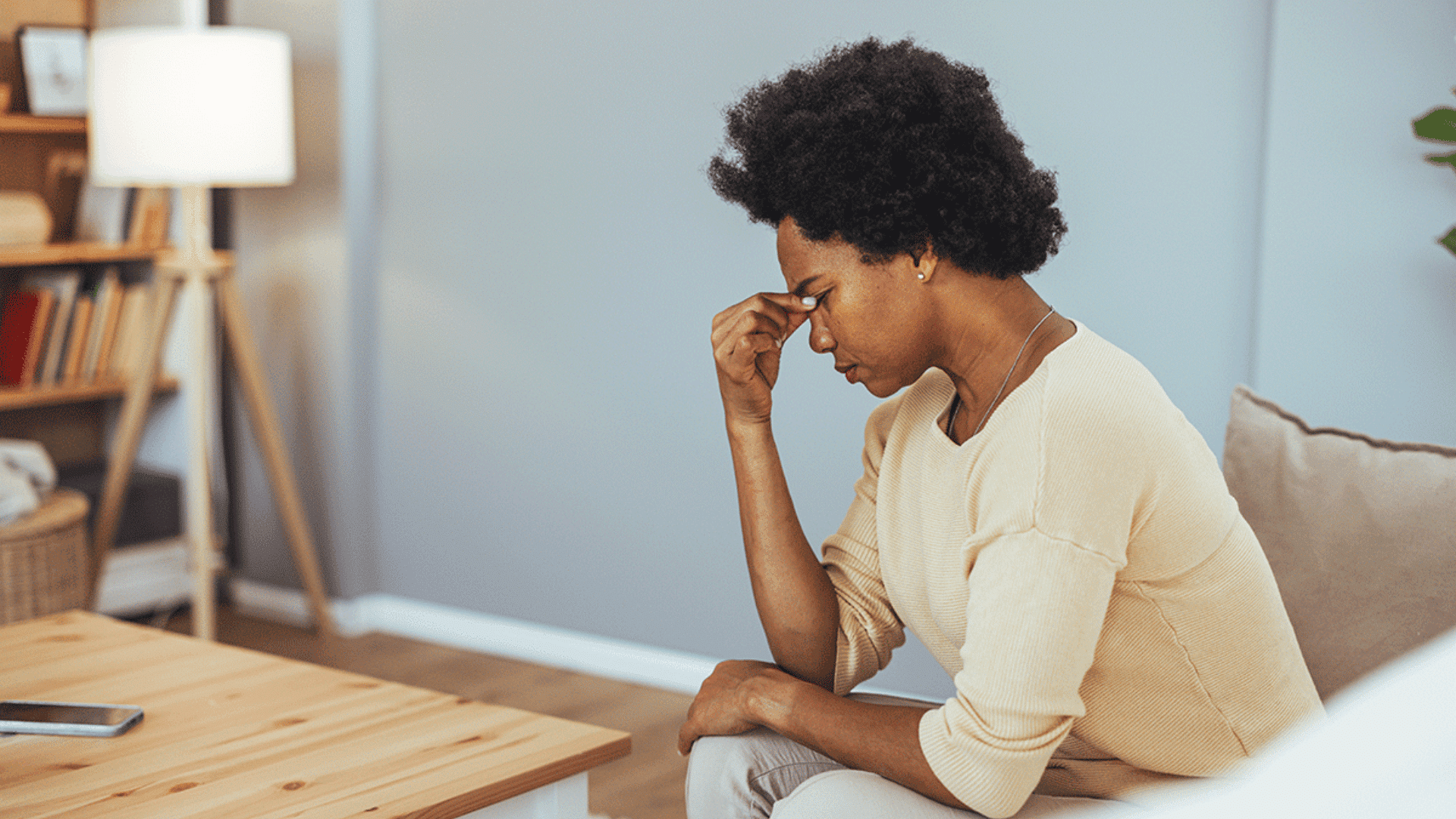 woman sitting on a sofa holding her forehead while feeling stressed in a quiet living room
