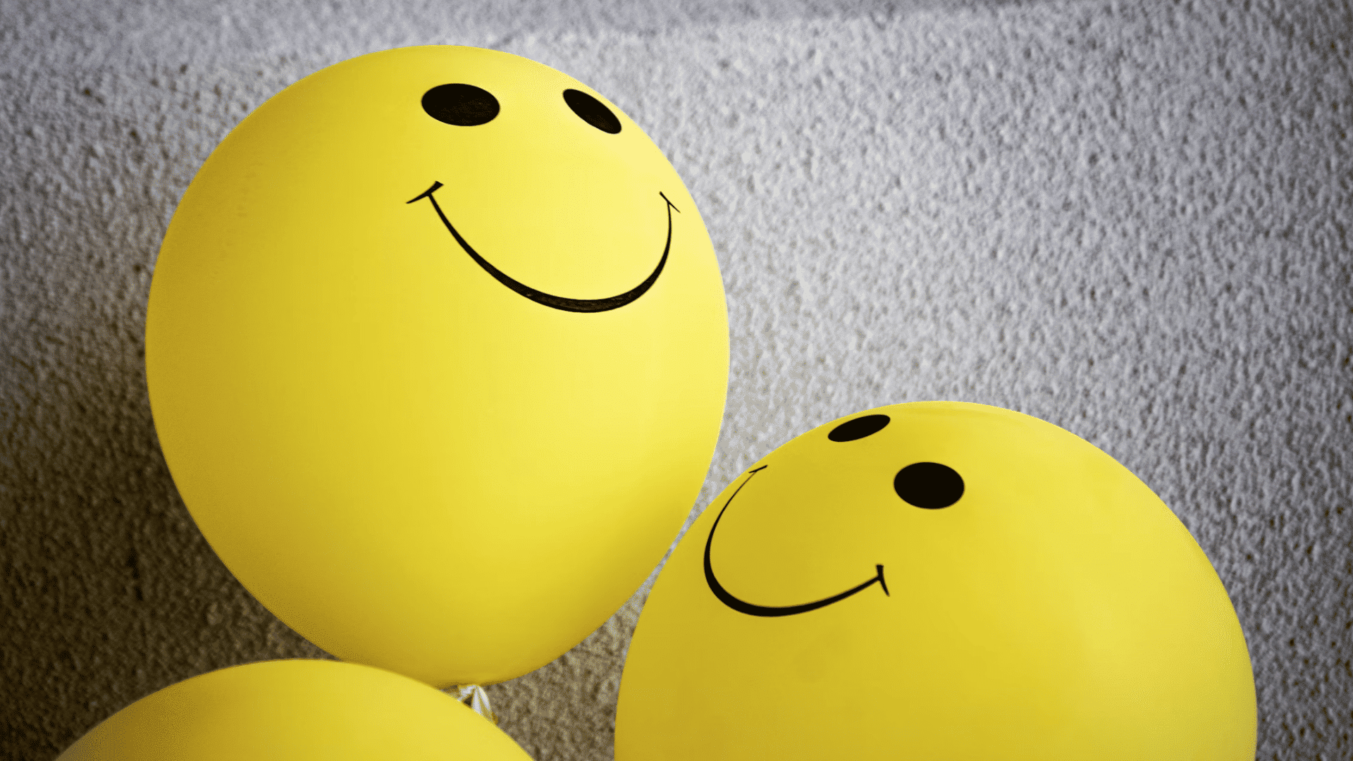 yellow smiley face balloons grouped together against a textured wall representing happiness and positivity