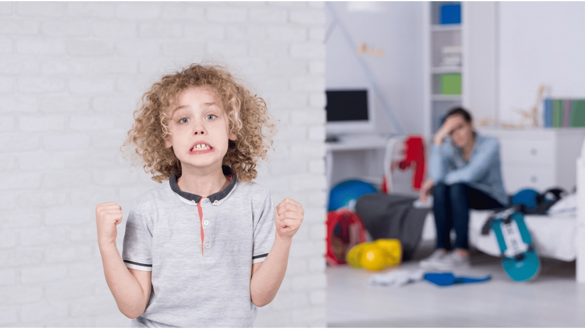 young child clenching fists with a worried expression while an adult sits blurred in the background