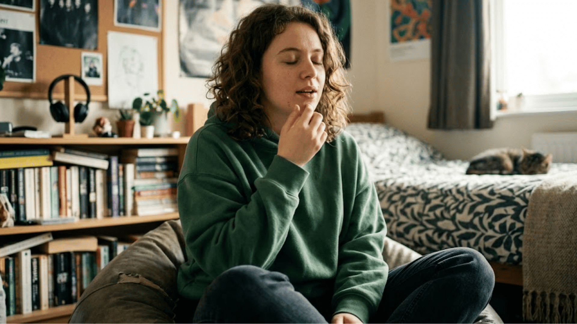 young person sitting cross legged on a beanbag in a bedroom with eyes closed practicing mindfulness near a bed