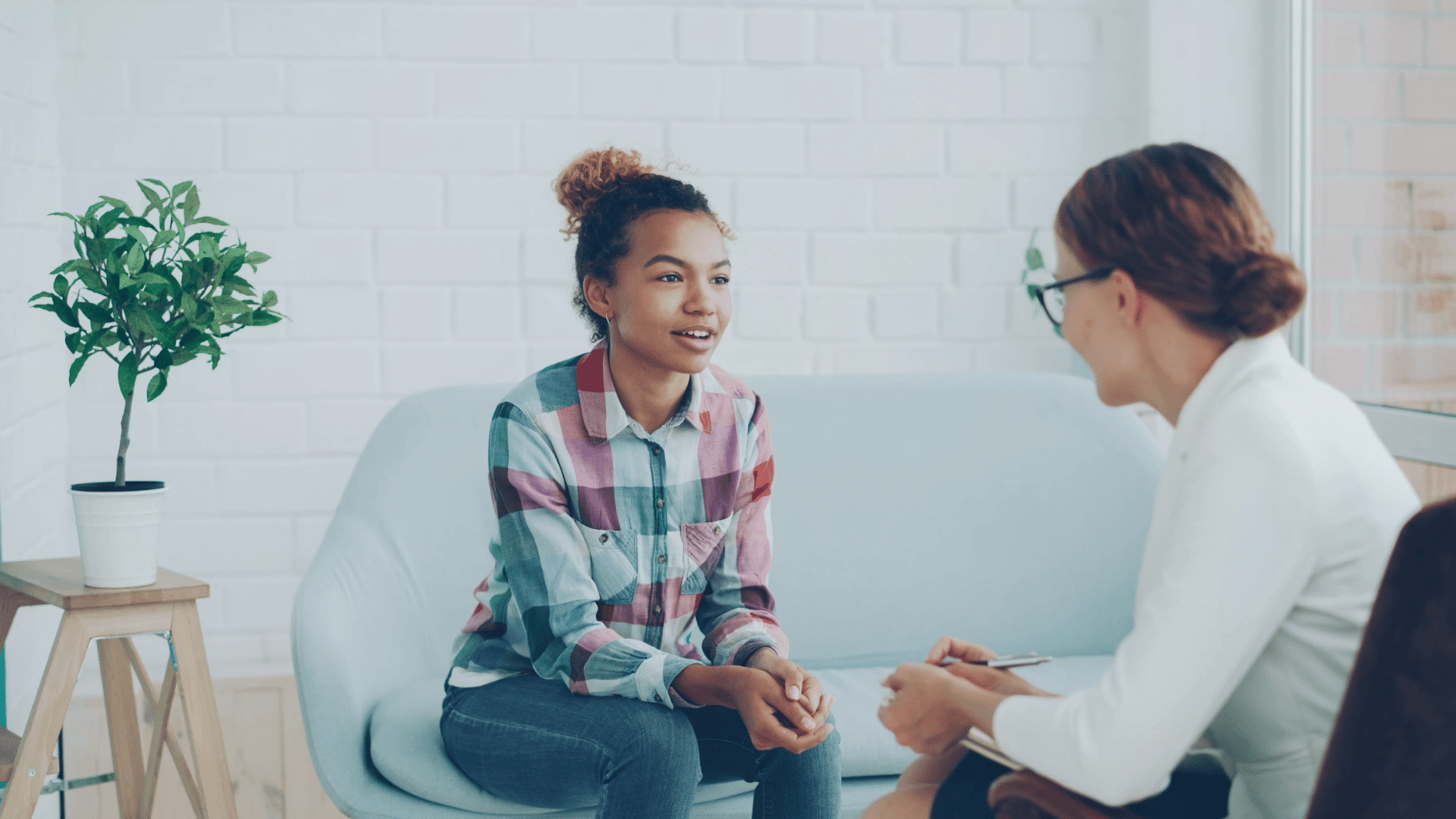 young woman speaking with a therapist during a counseling session while seated on a sofa in a bright office