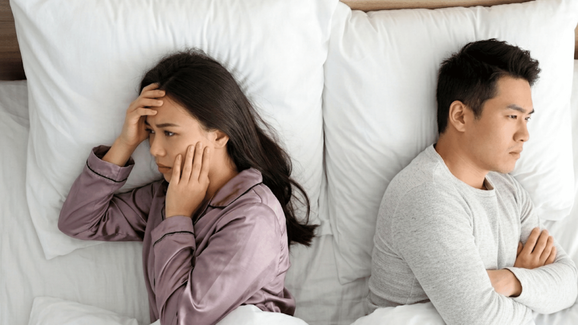 a couple lying apart in bed facing away from each other showing emotional distance and relationship conflict