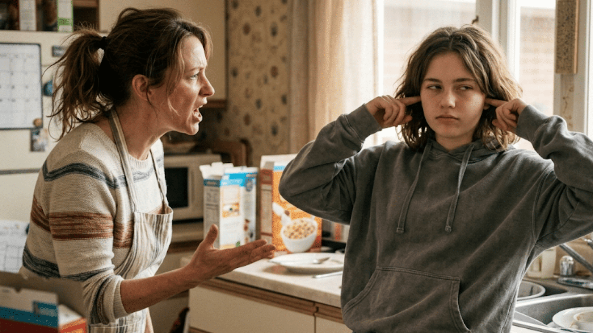 adult speaking firmly to a teenager in a kitchen while the teenager covers their ears and looks frustrated during an argument