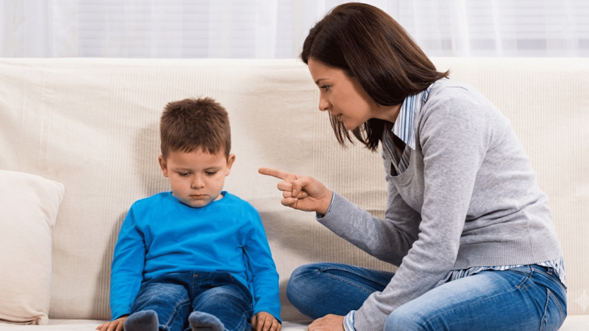 parent pointing while speaking to a young child sitting on a couch during a serious discussion